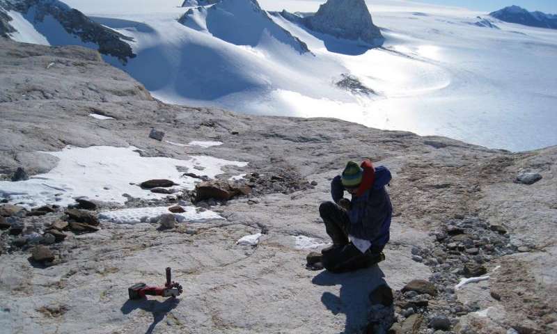 Um pesquisador examina rochas na paisagem da Antártida Ocidental
