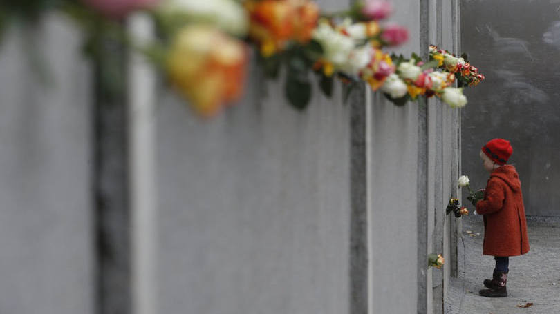 Menina coloca flores no memorial do Muro de Berlim